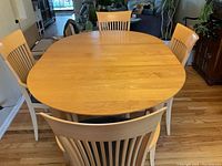 Top view of the oval light wood dining table with six chairs around it, showing slatted backs and natural wood finish