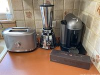 Photo showing KitchenAid toaster on the left, Osterizer blender in the middle, and Nespresso coffee maker with capsule box on the right.