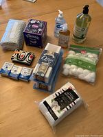 Photo showing all hygiene products including hand soaps, tissues, cotton swabs, cotton squares, and cotton balls neatly arranged on a wooden surface.