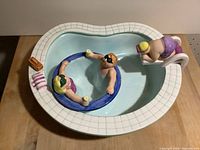 Large ceramic swimming pool shaped bowl with a diver on the diving board at one end and a smaller round bowl with two swimmer figurines inside.