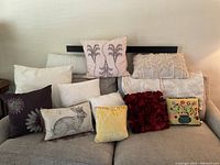 Full view of 12 assorted throw pillows and covers on couch showing variety of colors, patterns, and textures including botanical, rabbit illustration, ruffled rose, and embroidery.
