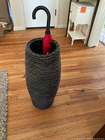 Wicker umbrella stand holding a red umbrella with a black hooked handle