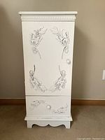 Front view of white cabinet showing butterfly embossed door and bottom drawer