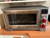 Front view of stainless steel oven with glass door, red knobs and digital display