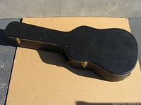 Closed guitar case showing top side with black exterior and gold latches