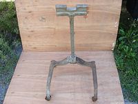 Outboard motor stand front view showing T-shaped top support and three-legged base with wheels on wooden surface against wood background.