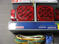 Two red square LED trailer lights with multiple LED bulbs, wiring harness and blue connectors on a blue box.