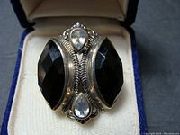 Close-up photo of sterling silver ring with two large faceted black stones and four smaller faint blue pear-shaped stones in decorative setting.