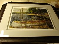 Framed print showing a canoe on a lakeshore with forest and mountains, titled "The Canoe".