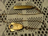 Photo showing the entire pocket watch fob cutter with attached chain and clip laid on a crocheted fabric background.