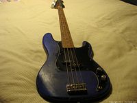 Full body view of blue painted Squire bass guitar with black pickguard, lying flat on a textured surface.