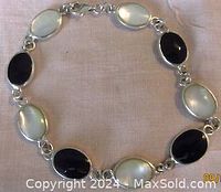 Top view of the bracelet showing alternating oval mother of pearl and black onyx stones bezel set in silver with lobster clasp.