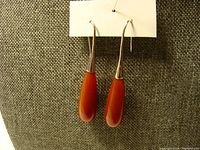 Full view of both teardrop-shaped reddish-brown stone earrings with sterling silver hooks against textile background.