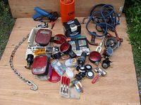 Overview of all items including trailer lights, electrical connectors, jumper cables, safety chain, vintage darts, and tools on a wooden surface.
