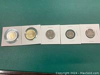 Photo showing five 2023 King Charles First Strike Canadian coins in 2x2 white holders: Toonie, Loonie, Quarter, Dime, Nickel, arranged in a row on a green surface.