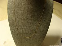 Full view of the thin gold necklace displayed on a dark fabric bust stand, showing overall length and delicate chain.