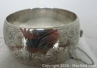 View of floral engraved sterling silver wide bangle bracelet showing shiny surface and detailing.