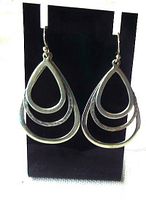 Pair of vintage sterling silver Silpada dangle earrings with nested tear drop design, one hammered and others smooth, hanging on black display stand.