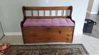 Front view of wooden deacons bench with tufted purple seat cushion on a patterned rug.