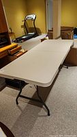 Full view of white plastic folding table set up in basement with metal legs and carpeted floor.