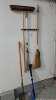 Photo of garden shovels, brooms, rake, and snow shovels hanging on garage wall
