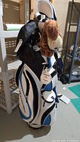 Full view of white/blue/black PowerBilt stand bag with clubs and plush headcover