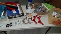 Photo showing six metal C-clamps in different sizes and two red spring clamps on a table along with boxes containing miscellaneous hardware items.