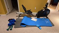 Full view of Freespirit 2-in-1 rower/recumbent bike with blue and gray exercise mats in front and blue sandals on mats.