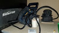 Photo showing the blue Mastercraft belt sander with black handle, power cord, and black carry bag with Mastercraft logo, also sandpaper rolls.