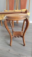 Side view of vintage wooden round side table with carved legs and lower shelf.