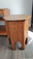 Front view of hexagonal wooden side table showing carved side panels and top surface.