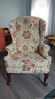 Front view of wingback chair showing floral fabric upholstery and wooden legs