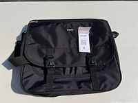 Front view of black Bugatti laptop bag with flap secured by two buckles and adjustable strap.