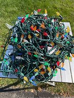 Bundle of outdoor decorative Christmas lights with multiple colored textured bulbs on green wiring shown in bright daylight.