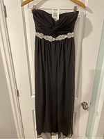 Full view of the black formal ceremony dress hanging on a door, showing the length and overall style.