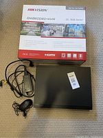 HikVision DS-7600 Series Embedded NVR unit with power adapter and wired mouse laid out front and original box behind