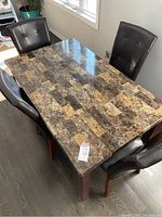 Overview photo showing the rectangular faux marble top table with four dark brown leatherette chairs in a kitchen setting with window light.