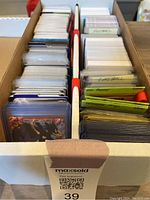 Top view of two-section divided box with traded cards sorted and sleeved, visible labels for baseball and football cards, and various trading card types.