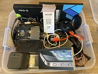 Mixed electronics and accessories in plastic bin showing charger, cables, iPhone box, and Q-Color device box.