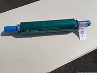 Full view of the green plastic wrap on white core with blue handle on each side.
