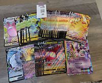 Mixed lot of jumbo Pokémon V, VMAX, and EX cards spread out showing holographic and foil effects with multiple copies of cards including Pikachu VMAX and Regidrago V.