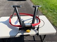 Saris Magnetic Indoor Bike Trainer shown from side angle resting on a white table with red resistance band attached.