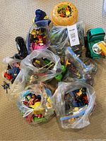 Top view showing multiple bags containing various figurines, toy vehicles, and small toys scattered on the floor.