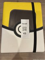 Front full view of the Ultra Pro Pokémon Ultra Ball trading card binder closed with black elastic strap, showcasing the large Ultra Ball design in yellow, white, black, and gray synthetic cover.