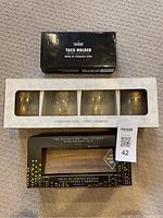 Full lot displaying boxes of 2 stainless steel taco holders, 4 wine glasses with pineapple logo in box, and Penalty Box 5 shot glasses with wooden tray in box.