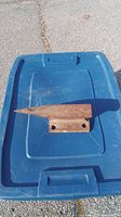 Top view of rusty small metal anvil placed on a blue plastic container lid showing tapered horn and mounting holes on base.