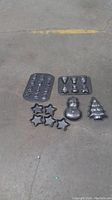 Photo of five different baking molds on concrete background: two flat pans with small molds, two star-shaped individual molds, and two 3D molds (snowman and Christmas tree).