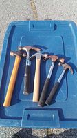 Full view of all five hammers arranged on a blue plastic surface showing varied handles and hammer types.