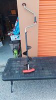 Full view of manual ice auger showing the crank handle, black auger shaft, and red handle grip.