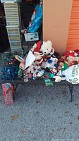 Wide view of assorted Christmas plush toys and decor arranged on a table including white bear, snowman, Santa, and reindeer plushes with other small festive items.